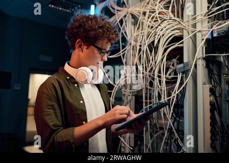 Serious young IT man working in data center standing at open server rack cabinet Stock Photo