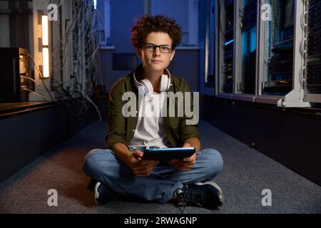 Teenager IT worker sitting on floor of modern server room working on tablet Stock Photo