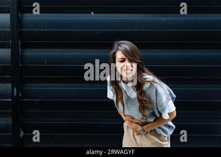 Business woman has severe abdominal pain during work with hand on stomach because nausea, painful disease feeling unwell. Ache concept menstruation an Stock Photo