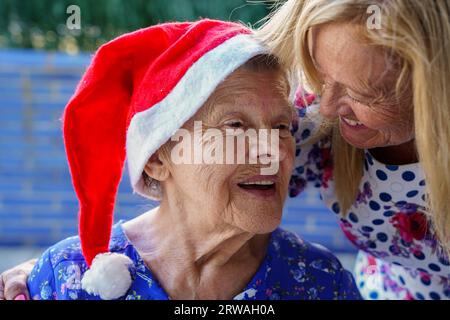 support and affection for old age at Christmas. A mature woman hugging her mother with a santa hat in xmas Stock Photo
