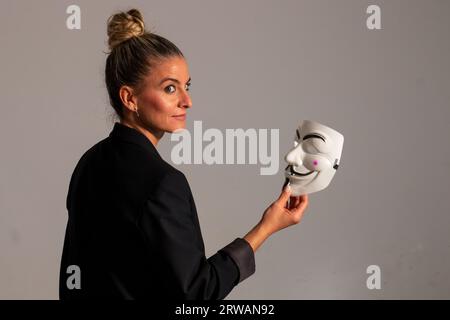 Woman with an anonymous mask dressed in a black colored suit jacket, carrying a knife in her hand, prepared for the Halloween party Stock Photo