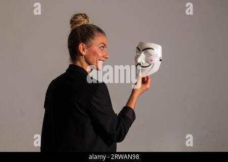 Woman with an anonymous mask dressed in a black colored suit jacket, carrying a knife in her hand, prepared for the Halloween party Stock Photo