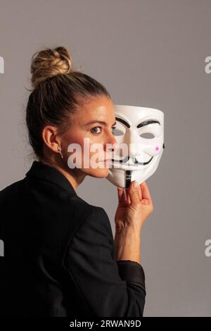 Woman with an anonymous mask dressed in a black colored suit jacket, carrying a knife in her hand, prepared for the Halloween party Stock Photo