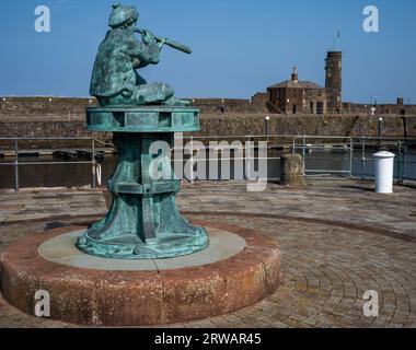 The 'Boy on a Capstan' looking across to the 18th century watchtower and Pier master's watch house, Whitehaven harbour, West Cumbria, UK Stock Photo