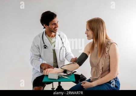 Asian doctor, from India, dressed in a white coat, measuring blood pressure on a redheaded European woman. Stock Photo