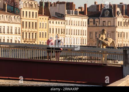 A couple pause on the Passerelle du Palais-de-Justice bridge next to the statue 'The weight of oneself' in Lyon France. Stock Photo