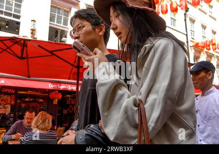 London, UK. Young Chinese couple in Chinatown. Woman checking her phone Stock Photo
