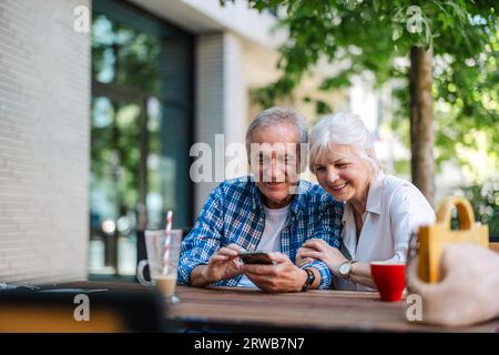 Senior couple sitting at a table in a cafe and using mobile phone Stock Photo