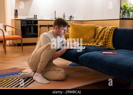 Focused IT guy sitting on floor with laptop working at home testes software websites digital product Stock Photo