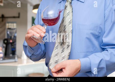 A man holding a wine glass in his hand and is letting some of vine drip onto his tie. Stock Photo