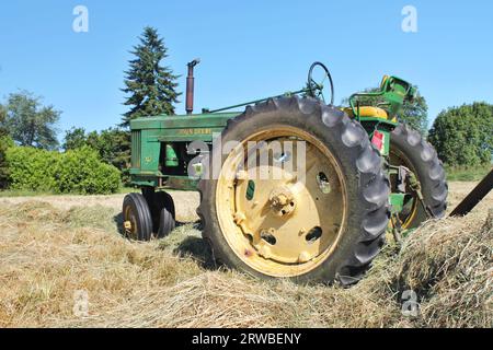 Vintage John Deere tractor with its iconic green and yellow paint colors sits idle in a hay field on a sunny day in the Pacific Northwest U.S. Stock Photo