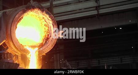Metal cast process in blast furnace in metallurgical plant or factory. Liquid iron molten metal pouring in container, heavy industry background Stock Photo