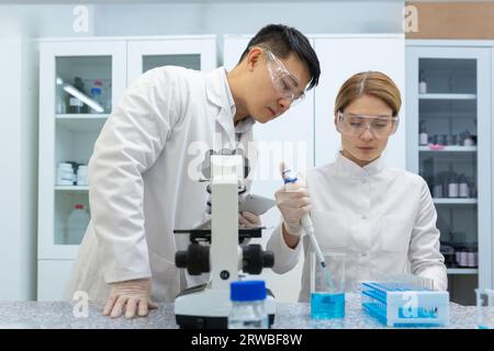 Two students, an Asian man and a young woman, are studying in a medical laboratory. They work at a table with liquid samples and examine them under a microscope. Stock Photo