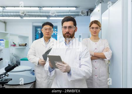 Portrait of self-confident scientists, doctors. An international team of a woman and two men standing with arms crossed in a laboratory and looking seriously into the camera. Stock Photo