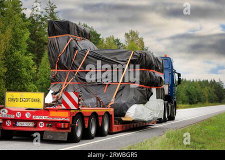 Scania truck low loader trailer hauls tarpaulin covered object as oversize load on road, rear view, focus on load. Raasepori, Finland. Sept 8, 2023. Stock Photo