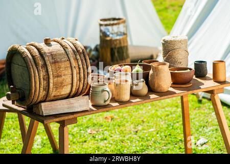 Food and drink set up on a table during a medieval re-enactment. Among the items are a wooden bowl of fruit, a keg, and wooden and clay cups. Stock Photo