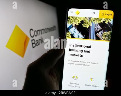 Person holding cellphone with webpage of company Commonwealth Bank of Australia (CBA) on screen with logo. Focus on center of phone display. Stock Photo