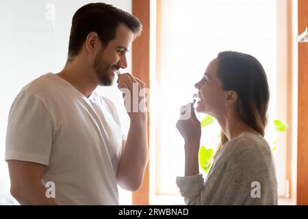 Happy young couple brushing teeth together, standing in bathroom Stock Photo