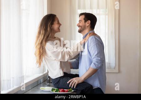 Beautiful woman sitting on countertop, having fun with husband Stock Photo