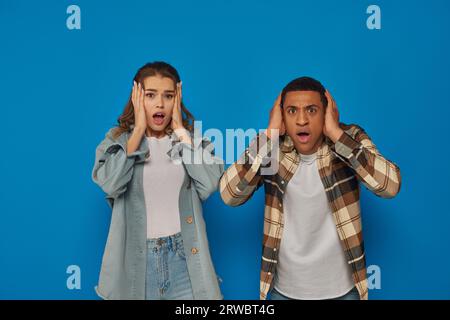 shocked interracial couple with open mouth looking at camera on blue background, emotional reaction Stock Photo