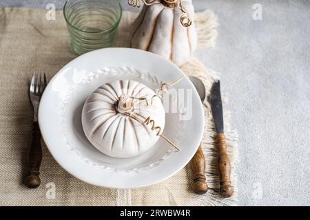 High angle of autumnal table setting with white pumpkin on plate placed on table near cutlery and glass Stock Photo