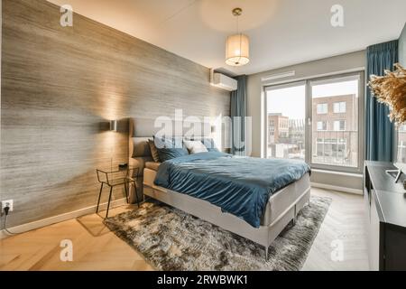 Interior of spacious bedroom with comfortable bed next to bright window with curtains on carpet and wooden wall in modern apartment Stock Photo