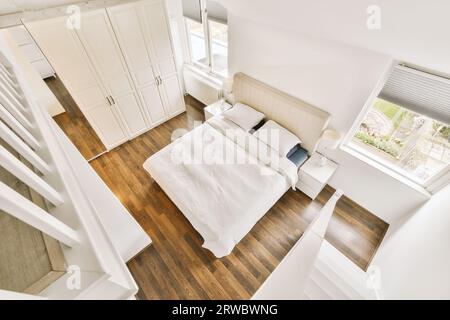 Overhead view of comfortable bed and large wardrobe placed next to bright windows in light spacious bedroom at home Stock Photo