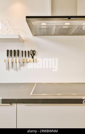 Interior of modern kitchen with various kitchenware hanging on white wall at countertop in light apartment Stock Photo