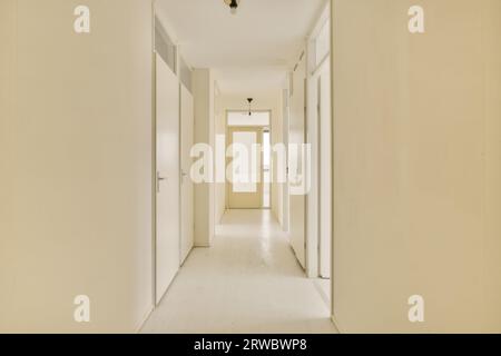 Interior of long narrow corridor leading to several rooms with white doors in modern house with beige walls and laminated floor Stock Photo