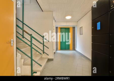 Interior of modern office building with empty hallway leading to green elevator and white tiles on floor Stock Photo
