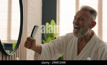Funny Caucasian old middle-aged retired elderly male senior mature man humorous silly carefree singing in hair brush sing song in hairbrush dancing Stock Photo