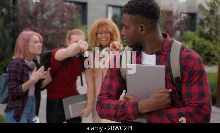 Sad upset offended victim boy student guy African American suffering man bullied of group multiracial students teens classmates thumb down mocking Stock Photo