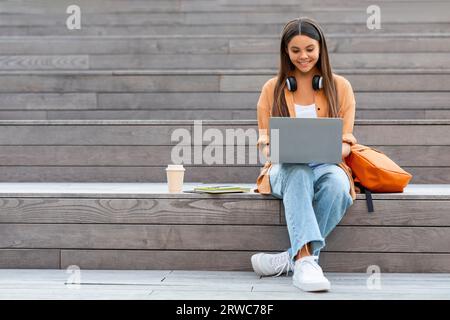 Cheerful young woman student working on project, using laptop outdoors Stock Photo