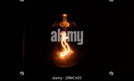 Glowing orange lightbulb in dark room Stock Photo