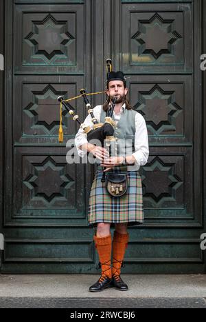 Bagpipe playerwearing kilt busking outside High Court of Justiciary, Royal Mile, Edinburgh, Scotland, UK Stock Photo