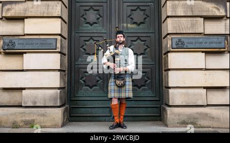 Bagpipe playerwearing kilt busking outside High Court of Justiciary, Royal Mile, Edinburgh, Scotland, UK Stock Photo