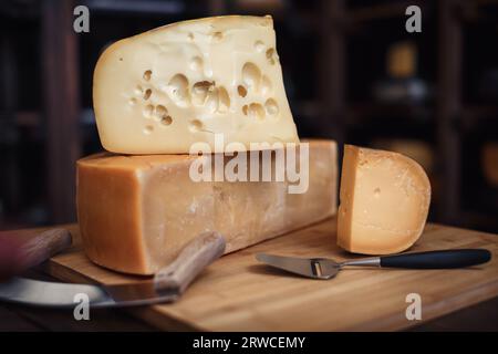 Cheese heads with slices and knives lie on a wooden board with an interior Stock Photo