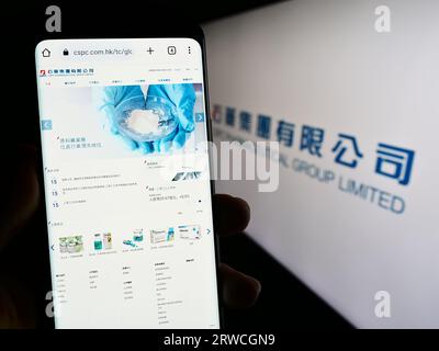 Person holding smartphone with webpage of company CSPC Pharmaceutical Group Limited on screen in front of logo. Focus on center of phone display. Stock Photo