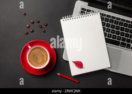 Blank notepad over laptop and coffee cup on office black table. Top view. Stock Photo