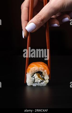 Hand holds sushi a chopsticks over a black table. Stock Photo