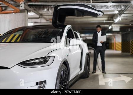 Electric motorcar being refueled by male with gadget indoors Stock Photo