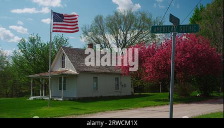 The iconic “American Gothic House,” made famous by artist Grant Wood, shares the frame with a blooming Crabapple tree and the American flag Stock Photo