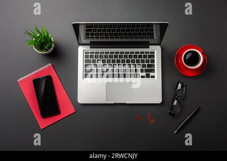 Black office desk table with blank screen laptop computer, notebook, mobile phone and red cup of coffee. Top view. Stock Photo
