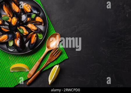 Seafood mussels and basil leaves in a black plate on bamboo mat and stone table. Top view. Stock Photo