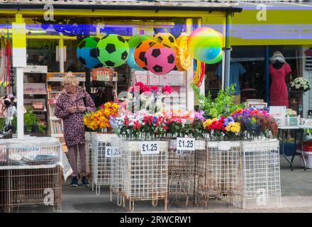 Colourful artificial flowers and beach balls on show on forecourt outside gift shop with lady looking at items cleveleys Lancashire England UK Stock Photo