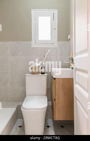 Vertical shot comfortable bathroom with a new renovation toilet bowl bathroom and sink new plumbing and stylish decor with a window in a european Stock Photo