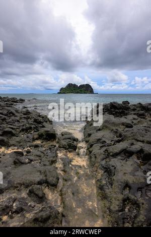 fiji island under blue cloudy sky across rocky beach Stock Photo