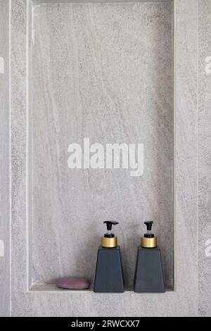 Two bottles of conditioner, shower gel on shelf in modern bathroom with textured wall Stock Photo