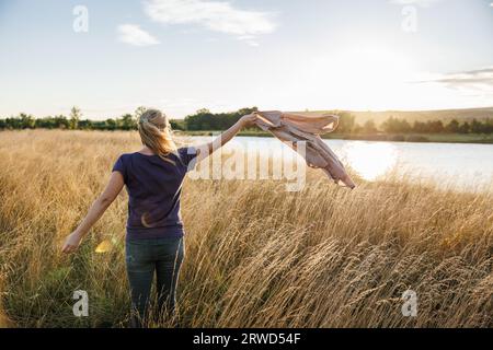 Woman standing in grass and enjoying windy weather at lake during autumn sunset Stock Photo