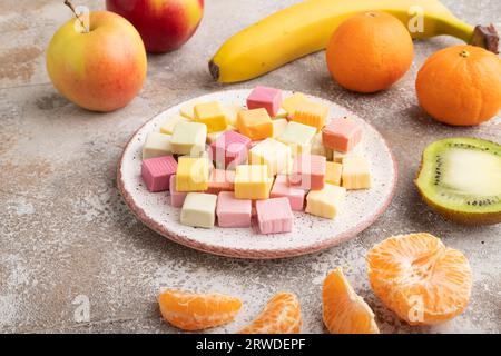 Various fruit jelly chewing candies on plate on brown concrete background. apple, banana, tangerine, side view, close up. Stock Photo